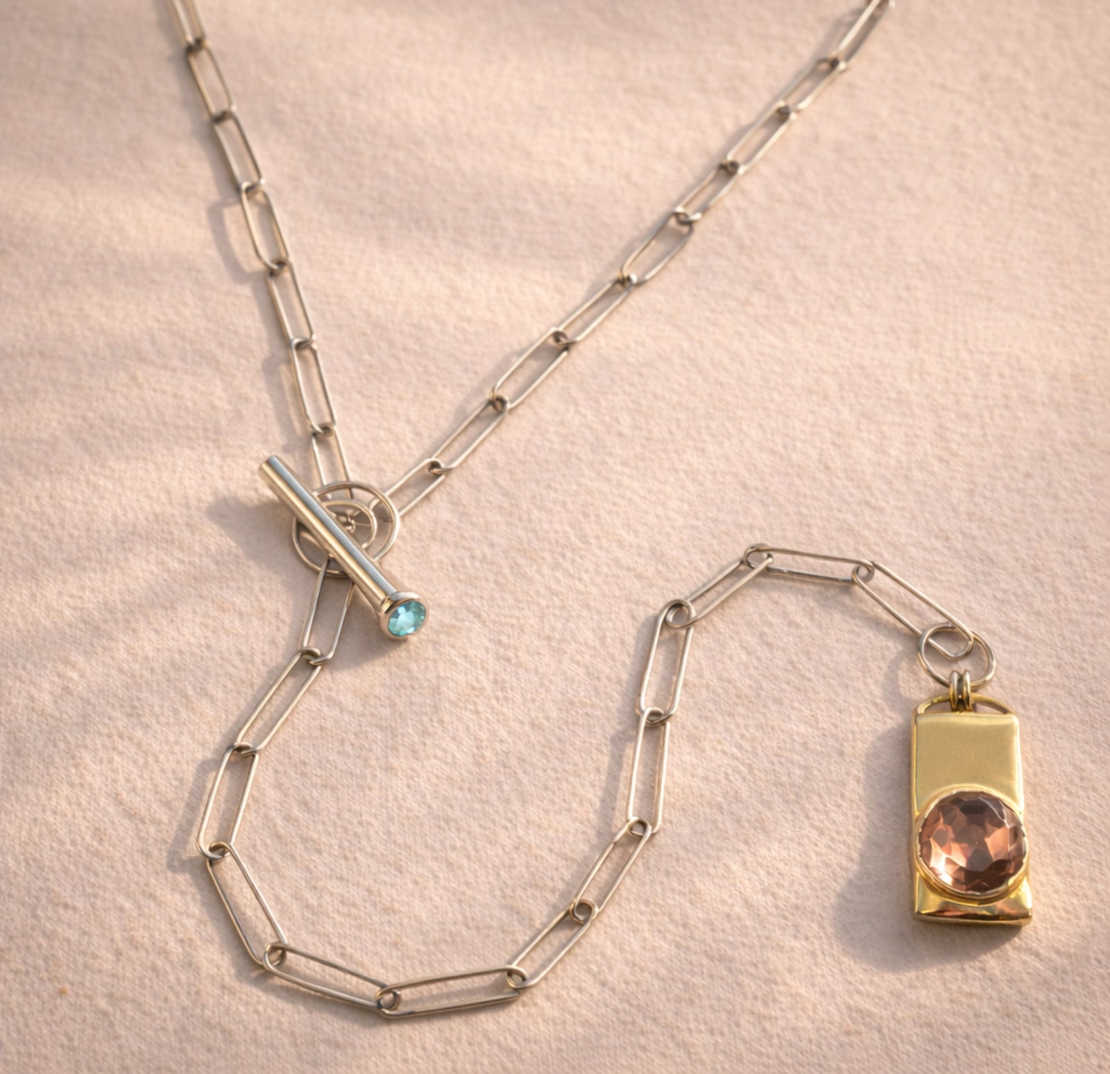 A close up of a custom Ruinette piece featuring a 10k yellow gold rectangle pendent with a smoky citrine brilliant cut, and a handmade sterling silver paperclip chain with a labradorite clasp