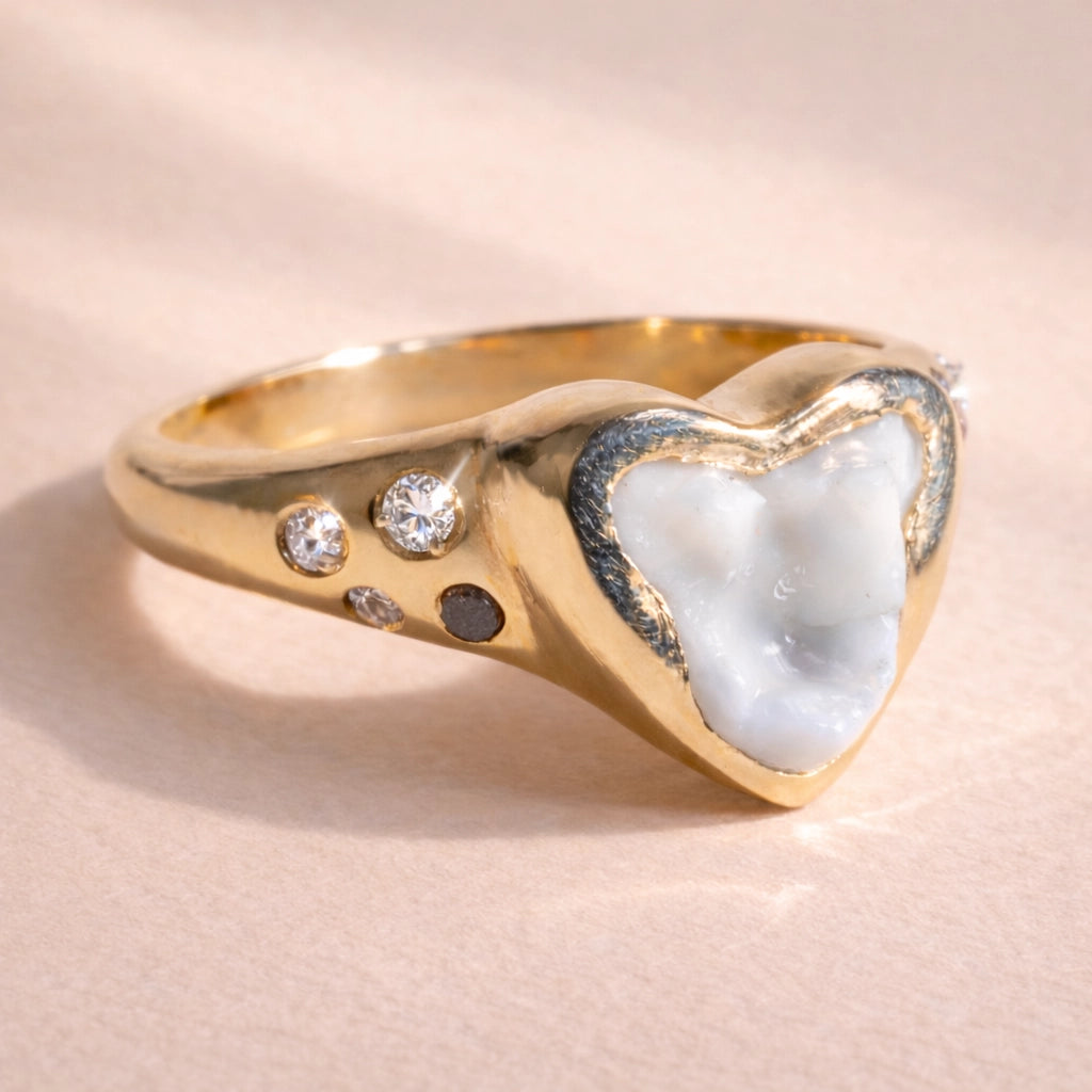 Close up of a custom signet ring by Ruinette, featuring a client's dog tooth with white and black diamonds, and pink tourmaline set in 14k yellow gold