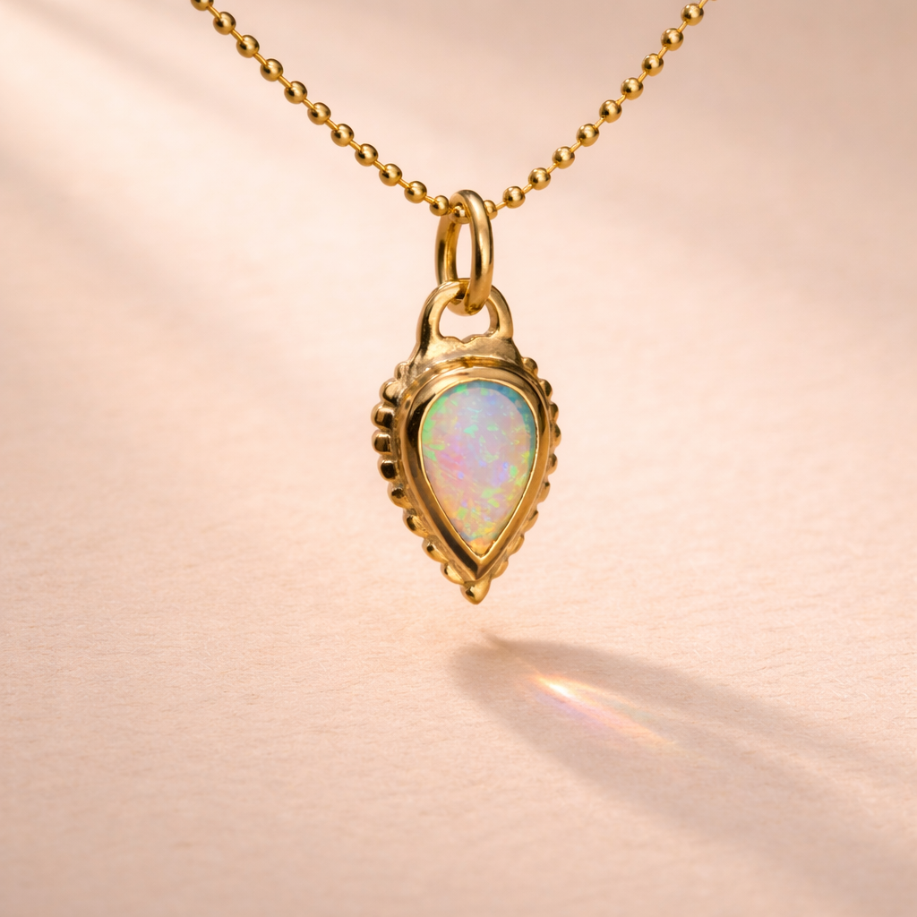An 18k yellow gold charm features an Australian opal pear cabochon, reflecting Ruinette Bijoux's artisan craftsmanship.