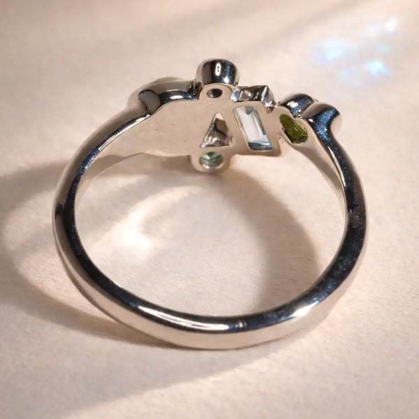 Ruinette Constellation Ring 1 shown from behind displaying the inside of an 18k white gold band with cluster of five gemstones in Sapphire, Aquamarine, Gray Moonstone, and Peridot.