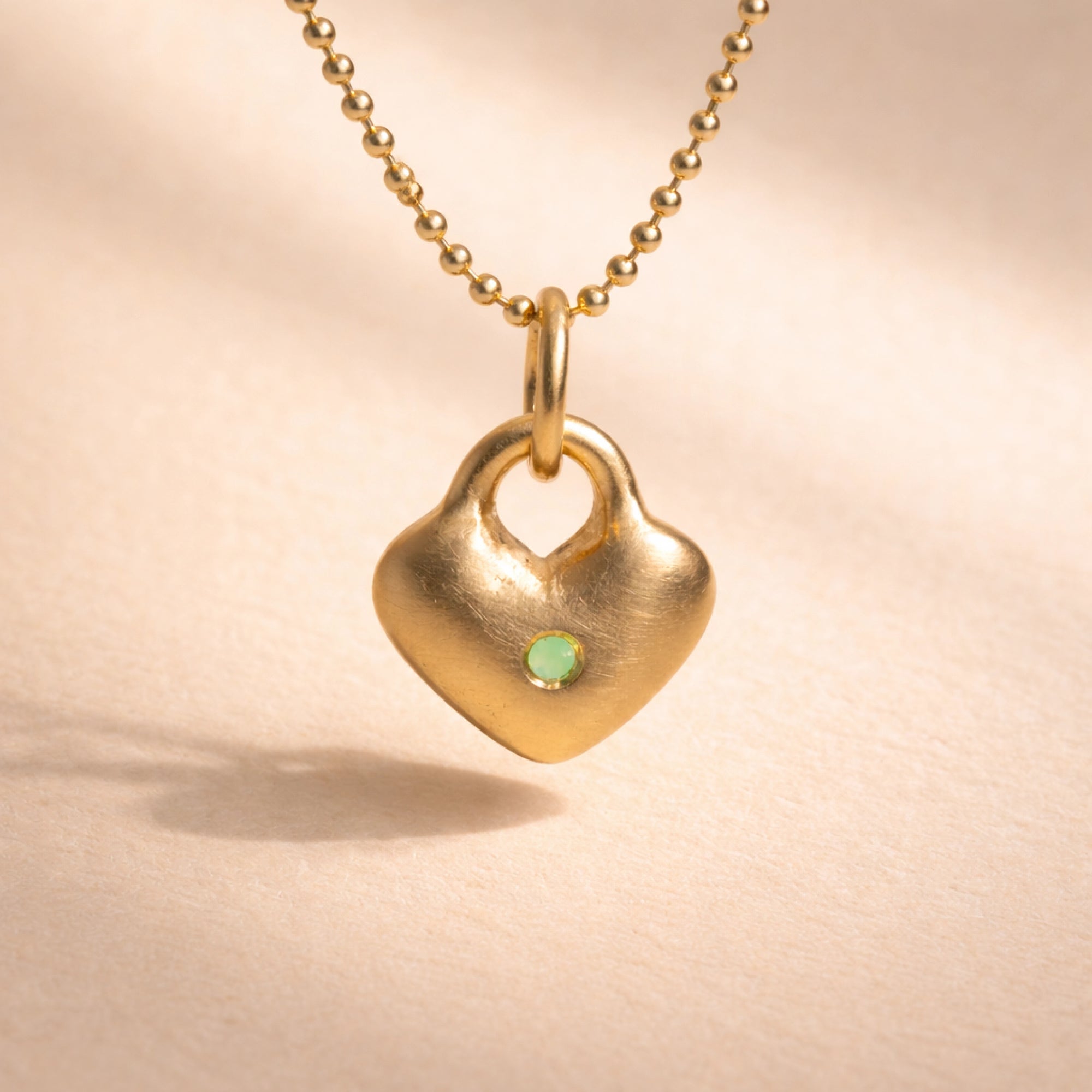 Ruinette Heart Charm close-up showing organic heart shape in matte 18k yellow gold with mint green chrysoprase cabochon center stone on ball chain