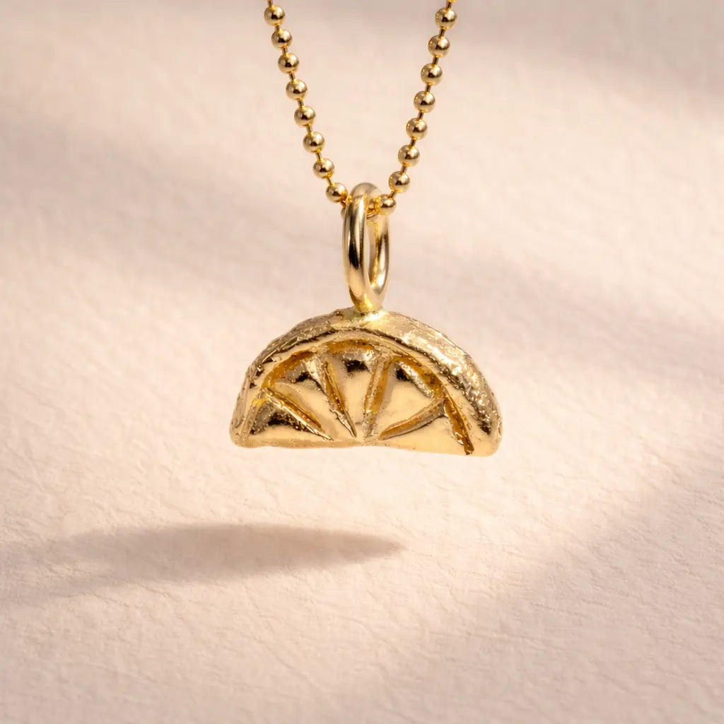 Ruinette Lemon Slice Charm in 18k yellow gold featuring textured exterior and geometric wedge pattern interior on ball chain, front view